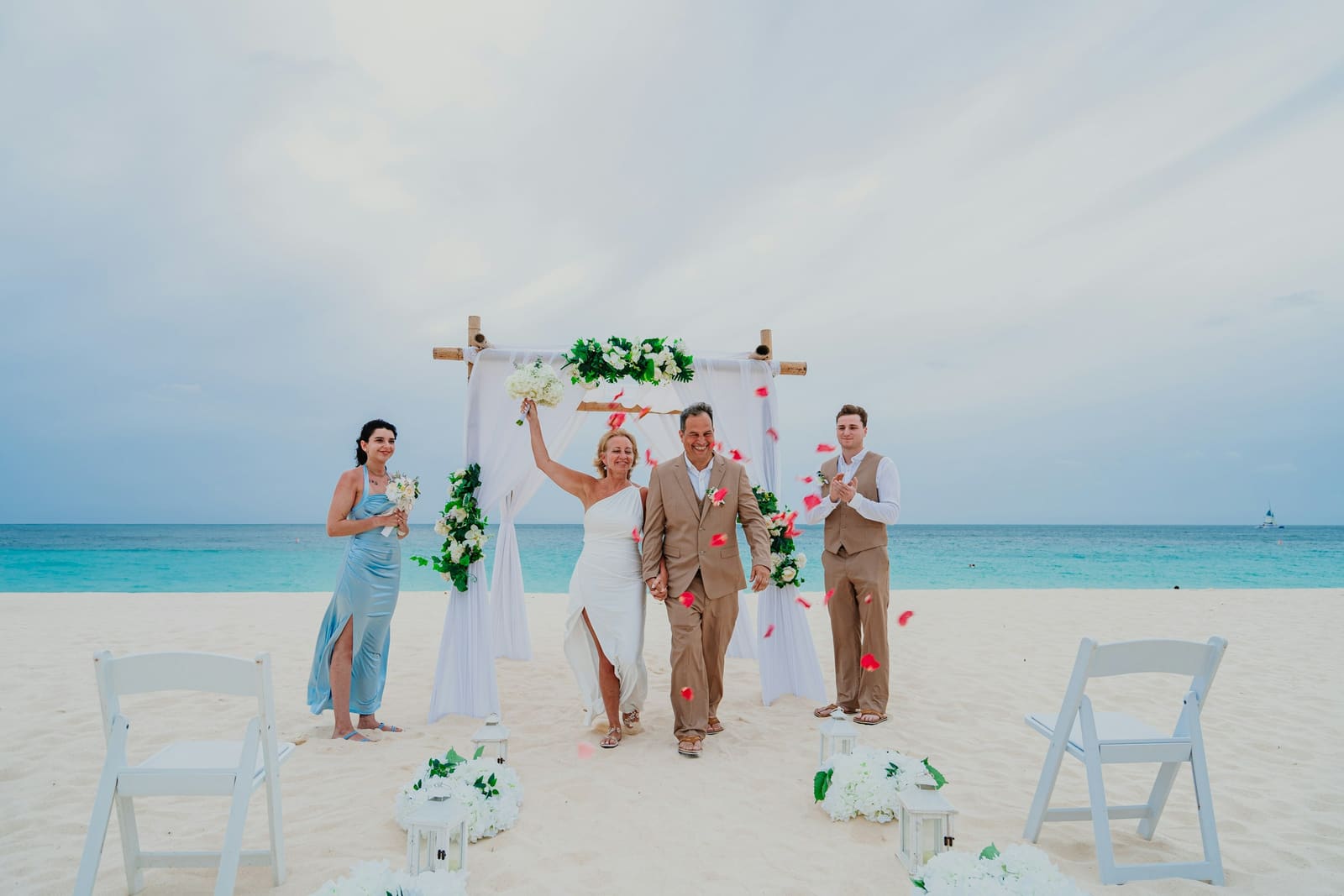 Newlyweds celebrate after a beach wedding ceremony with rose petals in the air